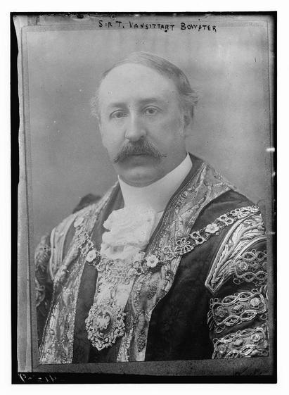 The image is a black-and-white portrait of a man, likely from the early to mid-20th century, judging by the style of clothing and the photographic technique. The man has a mustache and is dressed in formal attire that appears to be a ceremonial or official outfit. The garment is adorned with intricate embroidery and embellishments, featuring floral patterns and what looks like a badge or medallion on the chest. The background is plain and light-colored, which contrasts with the darker tones of the clothing. The image has a vintage appearance, with a border that suggests it might be a historical photograph. The name "SIR T. VANSITTART BOWATER" is inscribed at the top of the image, indicating that this is a portrait of Sir Thomas Vansittart Bowater, possibly a person of some prominence or official status. The overall tone of the image conveys a sense of formality and respectability.
