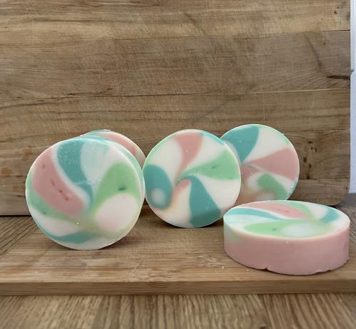 A collection of round, multi-colored soaps featuring swirls of pink, green, and blue, set against a wooden background.

Eine Sammlung runder, mehrfarbiger Seifen mit Wirbeln aus Rosa, Grün und Blau vor einem Holzhintergrund.