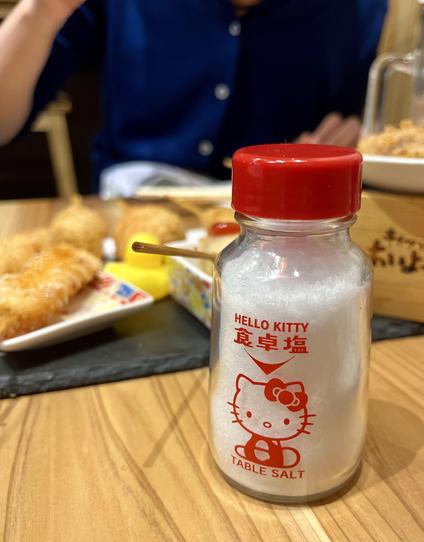 Ein kleiner Salzstreuer mit Hello Kitty-Aufdruck auf einem Tisch mit japanischem Essen.
