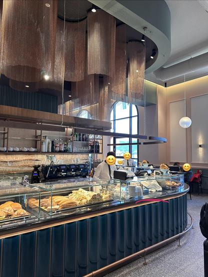A coffee bar with sandwiches. The bar has a curved shape, and above the bar, there are curtains of copper-coloured chain mail hanging from the ceiling, in similar curves