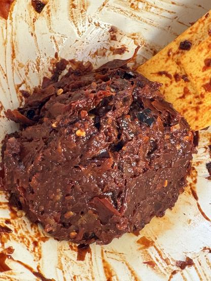 The sambal in the mortar. With a spatula on the right. It’s a brick red, with a few visible pieces of chili and some chili seeds.
The sambal is not cooked yet.