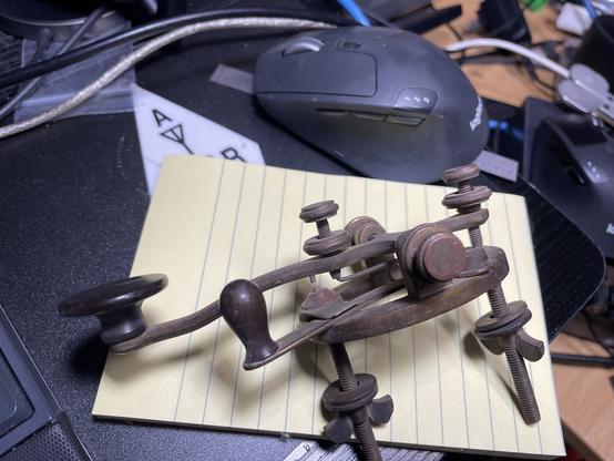 Side view of my Old brass straight telegraph key with a tension spring that looks like a safety pin. The base has two screws that can be used to mount the key to a table with the brass wing nuts.