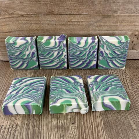 Colorful handmade soap bars display a marbled design featuring green, purple, and white swirls. They are arranged in two rows on a wooden surface.

Bunte handgemachte Seifenstücke zeigen ein marmoriertes Design mit grünen, lila und weißen Wirbeln. Sie sind in zwei Reihen auf einer Holzoberfläche angeordnet.