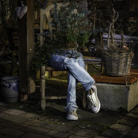 Eine Jeanshose die so ausgefüllt wurde als würde nur der Unterleib eines Menschen auf einem Stuhl sitzen incl. Turnschuhe. Da wo normalerweise der Korpus anfängt sitzt eine Schale mit Grünpflanzen. Sehr dekorativ das Ganze in einem Hinterhof platziert.