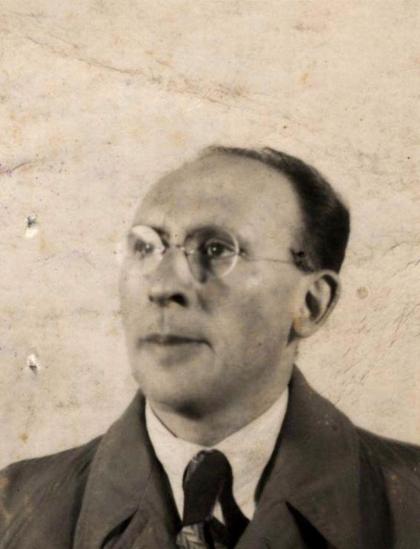 Vintage black and white portrait of a man wearing glasses, a suit, and tie, against a stained background.