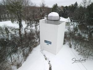 White observatory tower with a dome roof surrounded by snow-covered trees in a winter forest landscape.