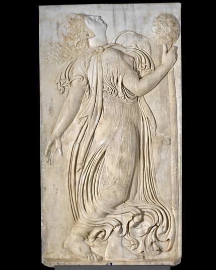 This relief depicts a maenad dancing wildly with her head thrown right back and her flowing gown swishing around her from the movement. She holds a thyrsus in her right hand, an object often connected with Dionysos in iconography.