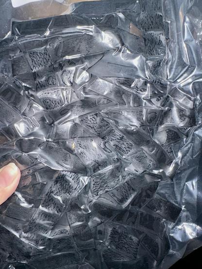 Vacuum pack plastic bag filled with something squished and black. My thumb shows as I held it up to take a cellphone photo with flash.