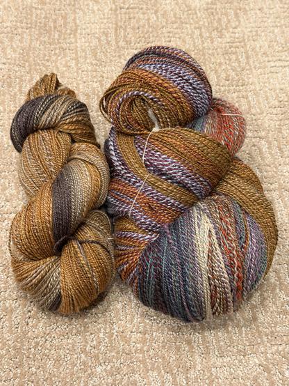 Two skeins of handspun yarn made of Haunui wool and Mulberry silk. Left skein is smaller and primarily browns, greys, golds. Right skein is large and has many colors from cold and purple and red. The plies are different colors shifting throughout