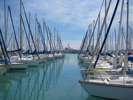Sailing yachts in the harbour of Antibes. Lined up on the left and right, and in the middle in the distance, a large motorised yacht.