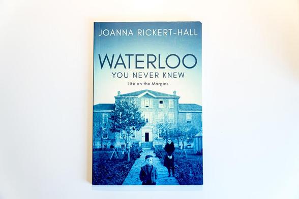 Photo of the cover of a book titled "Waterloo: You Never Know, Life on the Margins", featuring a vintage photo of two children standing in front of an old Victorian house.