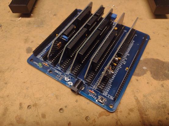 A mostly complete RC2014 Classic II 8 bit kit computer on a dirty MDF workbench. It has a blue backplane flush on the bench with eight "slots" - each a single row of pin sockets - and five small blue cards inserted.

There are various electronic components soldered to the boards, but all the chip sockets are empty.