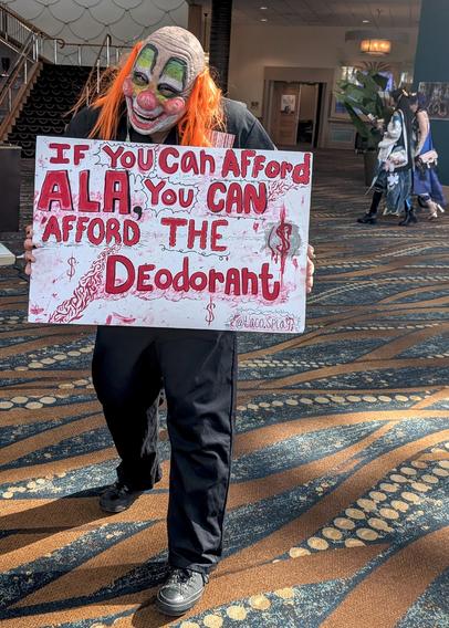 Cosplayer Taco.Splay holding a sign that read "If you can afford ALA, you can afford the deodorant."