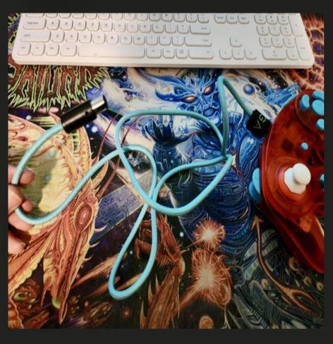 A custom transparent orange GameCube controller with white stick and turquoise buttons, with the turquoise paracord made by me front and centre. Background shows a mousepad with a really cool sci-fi/fantasy type design and a white keyboard can also be seen at the top.