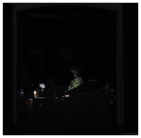 En fyrkantig, mörk bild tagen genom ett fönster. I mörkret sitter en docka av en soldat med hjälm och i uniform. Framför sig har han något för mig oidentifierat.