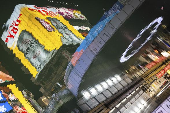 Water reflection in the dark of illuminated buildings covered in bright neons glowing in the dark and futuristic architectural elements in Osaka.