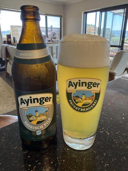 Bottle of Ayinger Pils next to a Ayinger branded glass filled with the beer and a nice ~3cm head