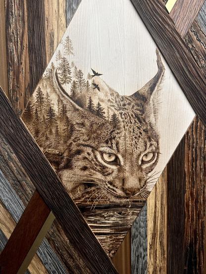 A woodburning of a lynx drinking water with a double-exposed foggy forest growing out of its back.