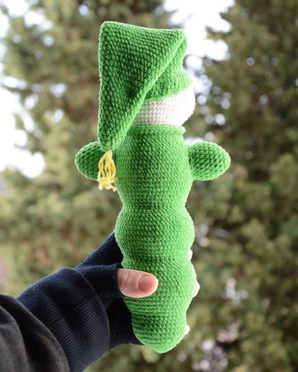 Luciole au crochet vue de dos, montrant sa forme allongée et son bonnet pointu vert, tenu dans une main, avec un arrière-plan naturel flou.
