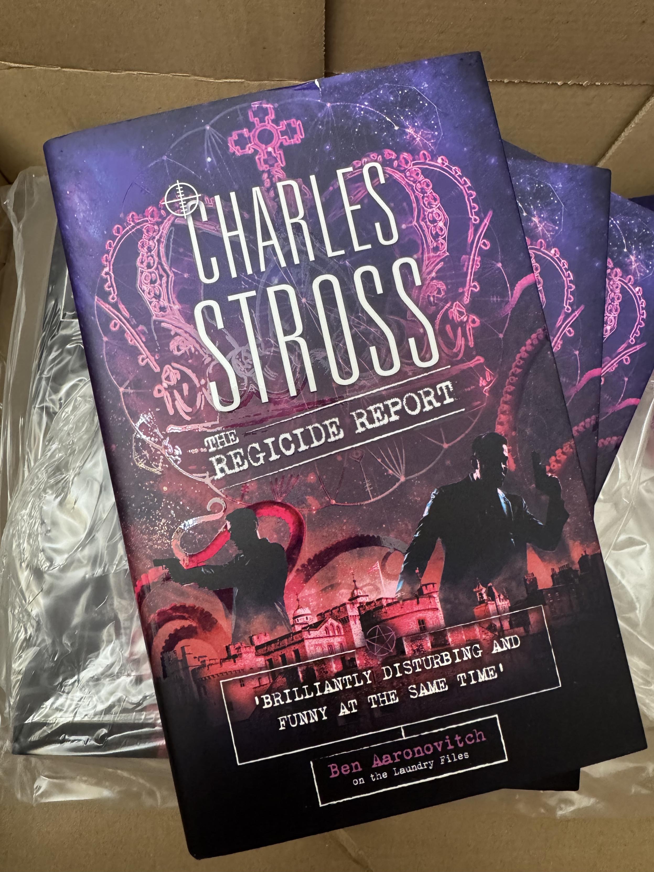 A pile of copies of a new hardcover titled "The Regicide Report" by Charles Stross, sitting in an open cardboard box.