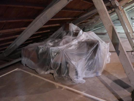 A pile of furniture and cardboard boxes in an attic covered with plastic film