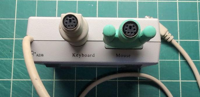The back of a platinum gray case with a cable hardwired into the left side, labeled ADB. The other two ports are labeled Keyboard and Mouse. Both ports have adaptors to use PS/2 devices in them, but the ports on the case are DIN and serial, respectively.