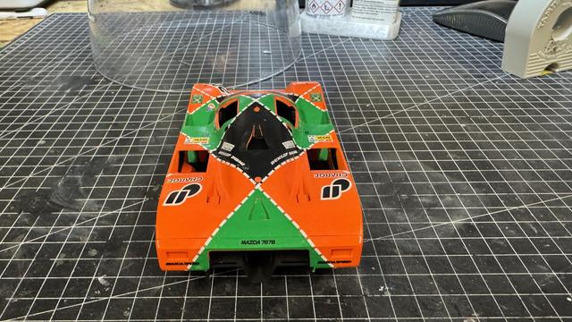 Rear view of Hasegawa Mazda 767B 1:24 model showing the rear wing, green undertray, and 'Mazda 767B' text on the chassis, photographed on a measurement grid mat