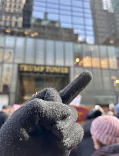 My gloved hand, showing its middle finger, with an out of focus Trump Tower in the background.
