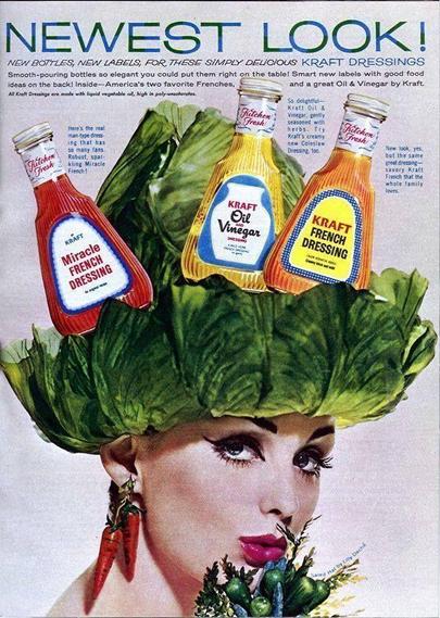 A full-page color magazine advertisement for Kraft salad dressings, likely from the early 1960s. At the center is a stylized portrait of a woman shown from the shoulders up against a pale background. She wears a dramatic, sculptural hat made entirely of overlapping green lettuce leaves that spread outward like a wide brim. Balanced on top of the lettuce “hat” are three glass bottles of Kraft salad dressing: Miracle French Dressing in a red bottle on the left, Oil & Vinegar in a clear yellow bottle in the center, and French Dressing in a red-orange bottle on the right. The bottles have newly designed labels and distinctive shapes. The woman’s makeup is bold and fashion-forward, with dark eyeliner and glossy lipstick. She wears novelty earrings shaped like vegetables, reinforcing the salad theme. Large headline text at the top reads “NEWEST LOOK!” with smaller copy below describing new bottles and labels for Kraft dressings. The overall design combines food packaging with high-fashion photography to present the product as modern and stylish.
