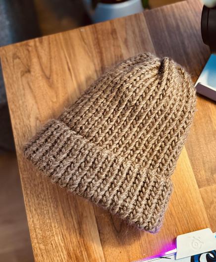 Valmis ruskeasta villalangasta neulottu pipo puisella pöydällä. Pipo on tehty loom knitting -tekniikalla ja siinä näkyy tasainen neulepinta.