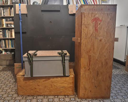 Three crates and a black wooden platform on a floor with coloured tiles, in what looks like an office.