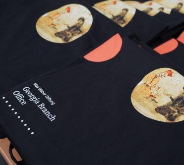 Stapel von schwarzen Jutebeuteln mit Aufdruck einer historischen Szene und weißem Text 'Georgia Branch Office'.