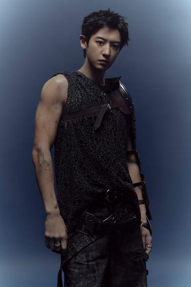 Chanyeol stares down into the camera wearing some kind of black mesh tactical gear with bare, dirty arms.
