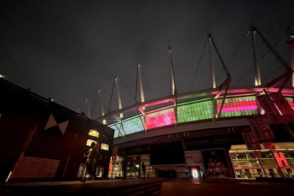 La imagen muestra un estadio iluminado por la noche, con luces de colores y una arquitectura moderna.