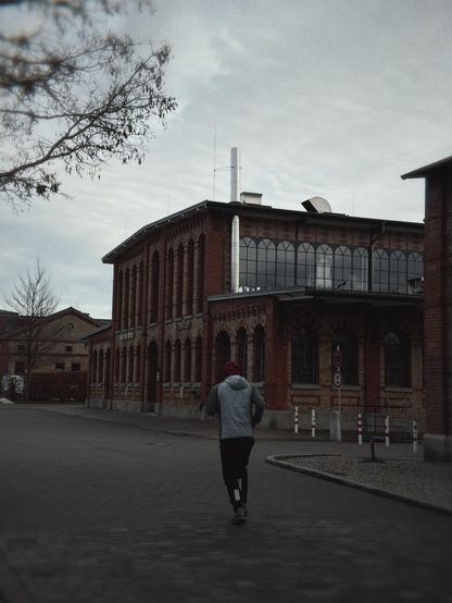 A person jogging on a paved street near a red brick building under a cloudy sky.