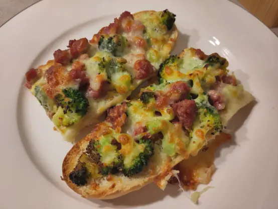 eine halbierte Baguettehälfte, die mit gebratener Salsiccia und Brokkoli belegt und mit Käse überbacken wurde.