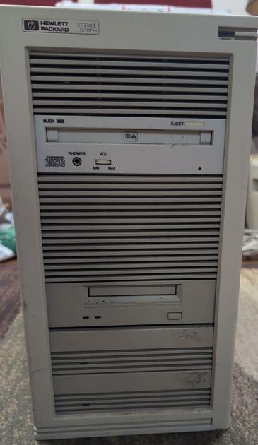 A gray computer tower with the HP logo in the upper left and an LED in the upper right. The entire front is 5 1/4" drive bays. The top one is blanked off, the second has a caddy CD-ROM drive, the next two are blanked off, the fifth has a tape drive, and the bottom two each have an LED for a hard drive.