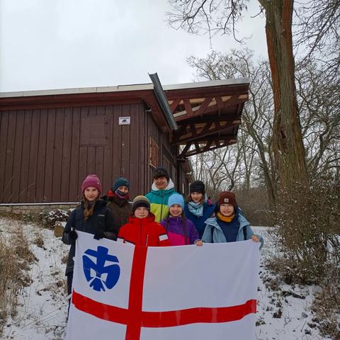 Unsere Teilnehmenden am Winterhaik stehen vor unserm Pfadfinder-Stammenshaus (der Georgsburg https://www.georgsburg-erfurt.de ) und halten die Fahne von unserem Pfadfinderverband (Deutsche Pfadfinder*Innen Sankt Georg) vor sich.