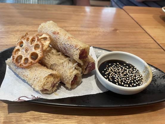 4 tarro spring rolls sit on a plate with 2 lotus stem deep fried pieces and a dark sauce.