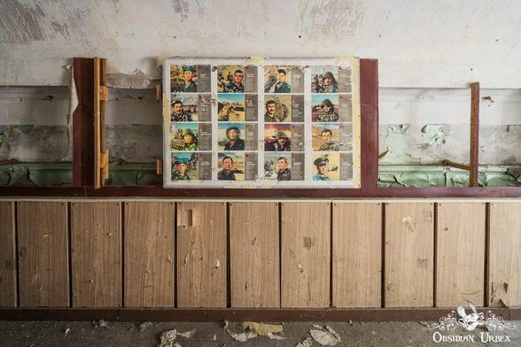 In an abandoned room, a wall displays portraits of Soviet-era military personnel on a deteriorating wall, accented with wooden paneling.