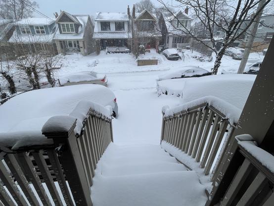 Photo of snow-covered stairs leading from a porch to a snow-covered driveway and street in Toronto’s East End.
