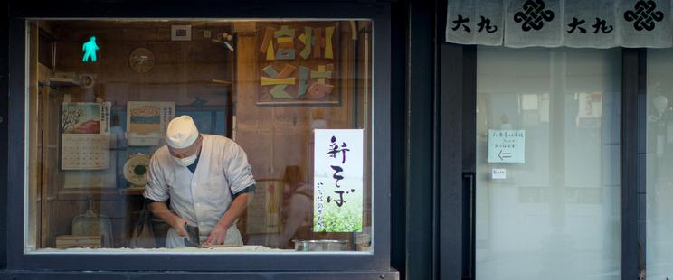 Anamorphic panoramic photo of a Soba chef making noodles in the window of his restaurant in Nagano.