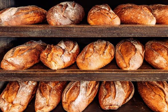 Varias hogazas de pan rústico en unos estantes de madera en el interior de una panadería (Getty Images)