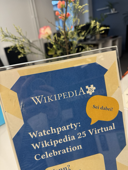 Schild mit dem Text: Wikipedia 25. Watchparty: Wikipedia 25 Virtual Celebration. Rechts oben eine Sprechblase, in der steht: Sei dabei.