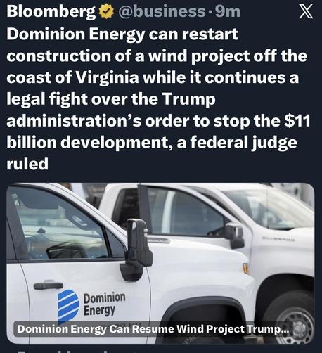 Image shows a close-up of a vehicle with the Dominion Energy logo. Several other white vehicles are visible in the background. The context relates to a federal judge's ruling allowing the company to continue a wind project off the coast of Virginia.