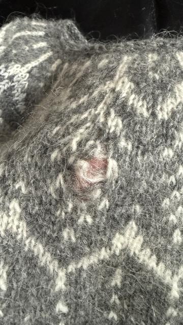 Ein größeres Loch in der Rundpasse eines handgestrickten Islandpullovers in dunkelgrau mit weißem Einstrickmuster, auch aus Plötulopi.