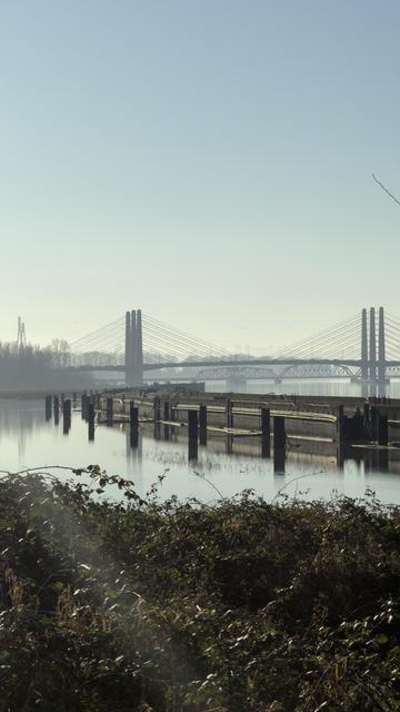 A decrepit concrete structure in a river near a cable bridge.