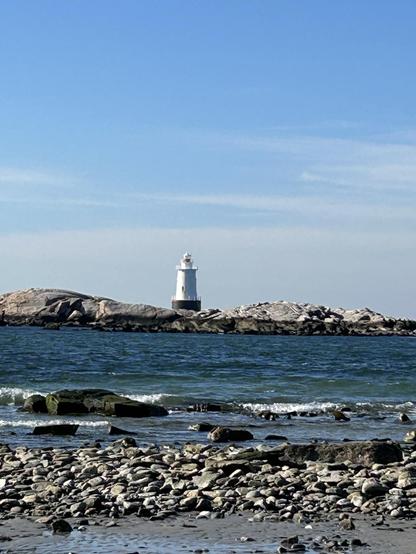 A lighthouse sitting on a rock across a beach and water.