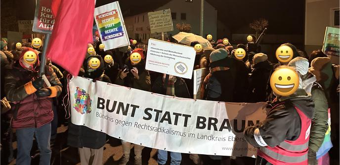 Photo der Demo. Vorne ist ein größeres Banner von „Bunt statt Braun“ zu sehen. Drumherum und dahinter viele Menschen mit Plakaten gegen Rechts. Die Gesichter sind zum Schutz der Privatsphäre mit einem Emoji überlagert.