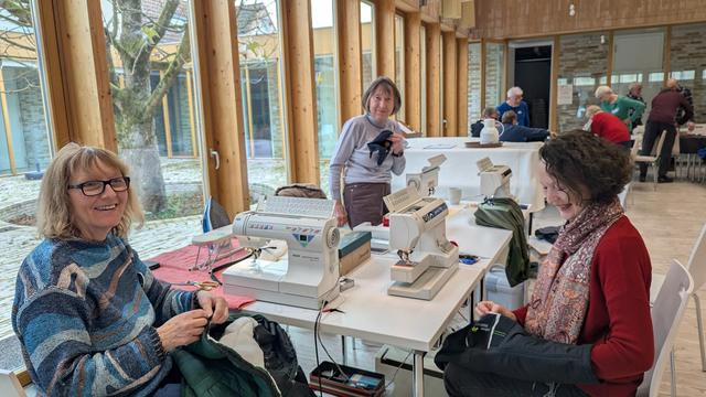 Im großen Saal der Petrusgemeinde stehen an mehreren zusammen gestellten Tischen 4 Nähmaschinen. Daran sitzen die Ehrenamtlichen des Werkstatt-Cafés nähen und haben Spaß!